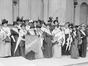 A black and white photograph of a group of suffragettes holding a Pennsylvania flag.